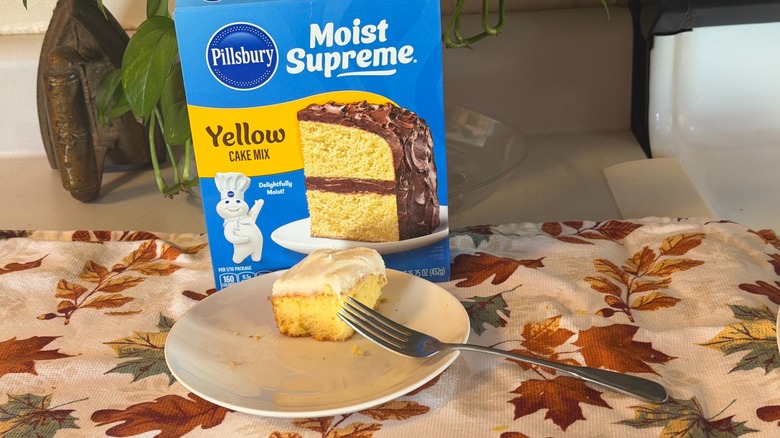 A piece of Pillsbury yellow cake with cream cheese frosting on a plate with a fork in front of the box.