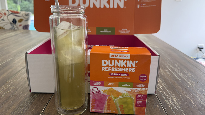 Dunkin' Kiwi Watermelon Refresher in glass with ice next to box of mixed drink sticks