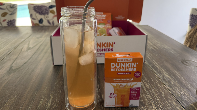 Dunkin' Mango Pineapple Refresher in glass with ice next to box of mixed drink sticks