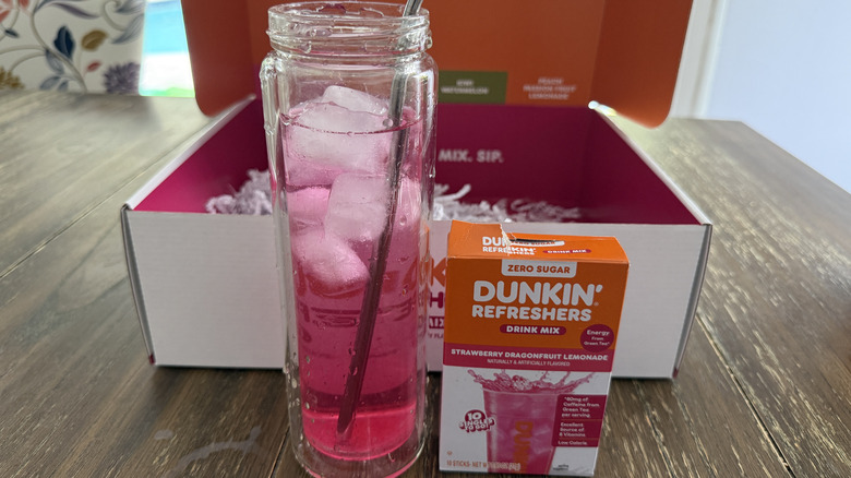 Dunkin' Strawberry Dragonfruit Lemonade Refresher in glass with ice next to box of mixed drink sticks