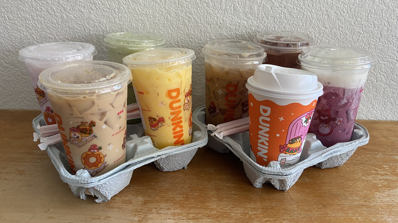 All eight Dunkin drinks in drink holders on a wood table.