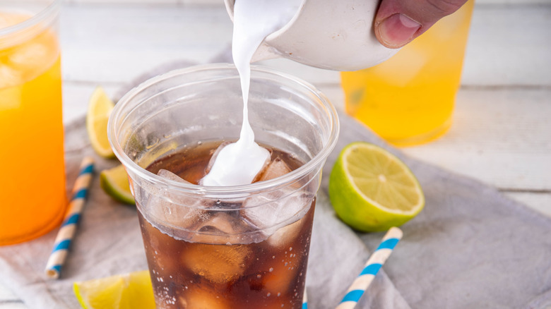 A person adding cream to a plastic cup of soda to create a dirty soda