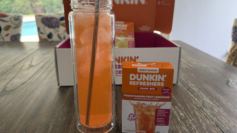 Dunkin' Peach Passion Fruit Lemonade in glass with ice next to box of mixed drink sticks