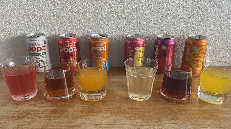all six cans behind glasses full of each soda