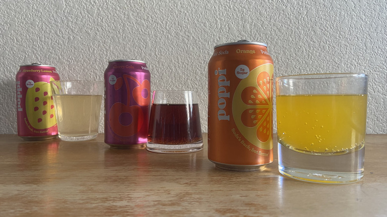 Poppi cans arranged diagonally beside glasses full of each soda