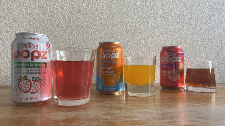 Popz cans arranged diagonally beside glasses full of each soda