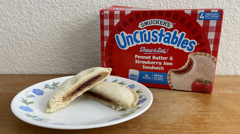 a halved Uncrustable on a plate with its box in the background