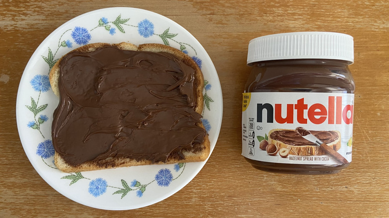 Nutella jar beside Nutella spread on a piece of bread
