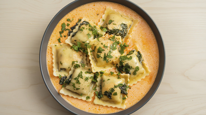 A bowl of ravioli with a creamy tomato-based sauce and fresh chopped herbs