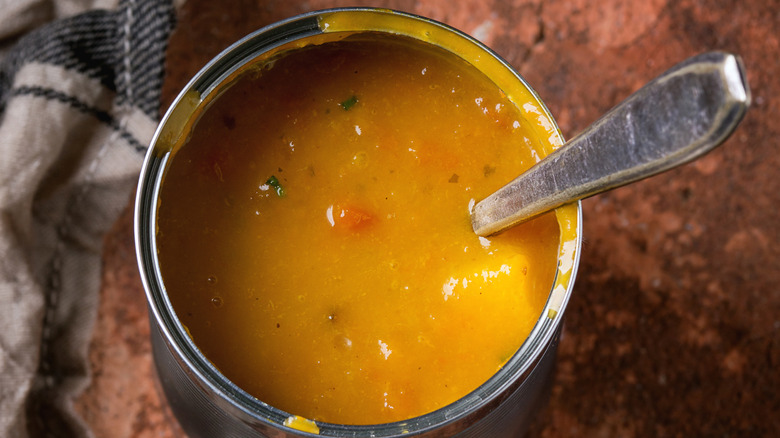A can filled with thick soup broth with a spoon and a kitchen towel