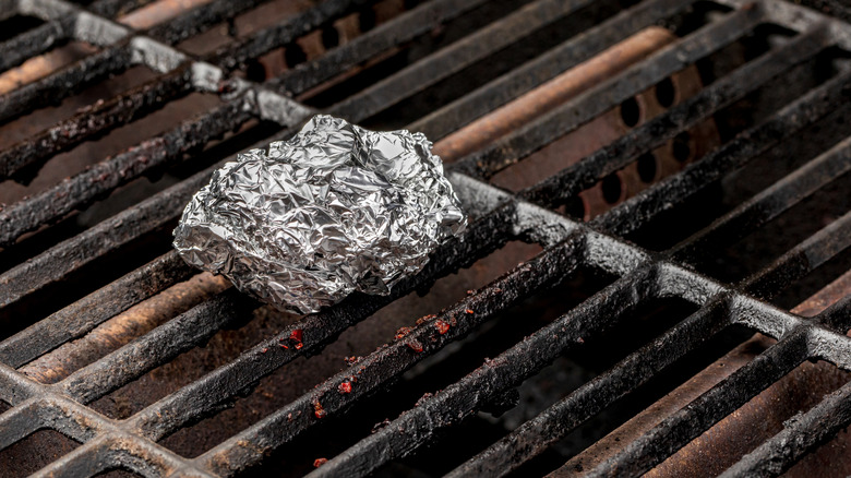 A ball of aluminum foil rests on dirty grill grates