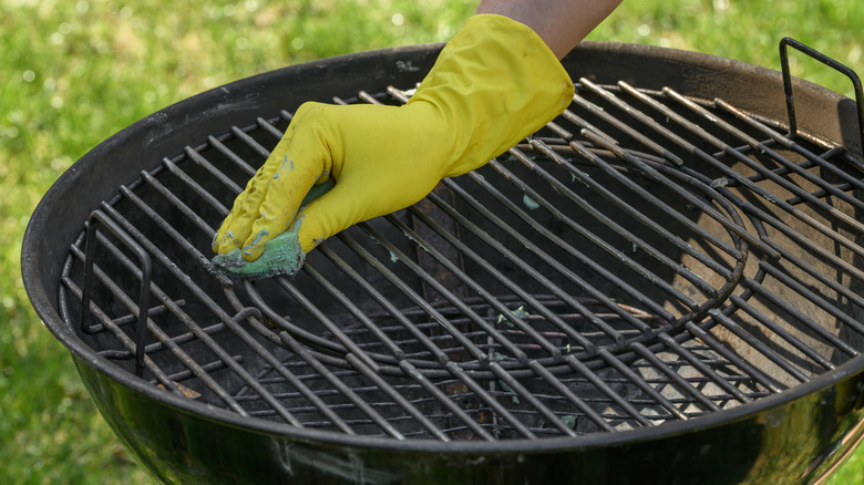 A hand in rubber glove wipes charcoal grill grates