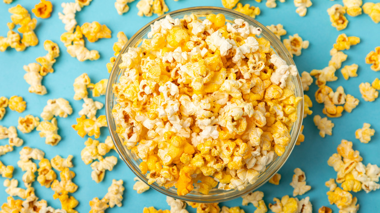 A clear bowl of popcorn against a blue background.