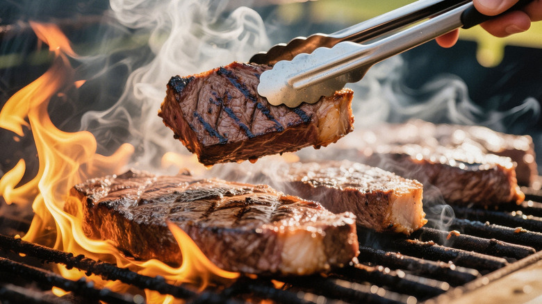 Tongs flipping steaks on grill with flames