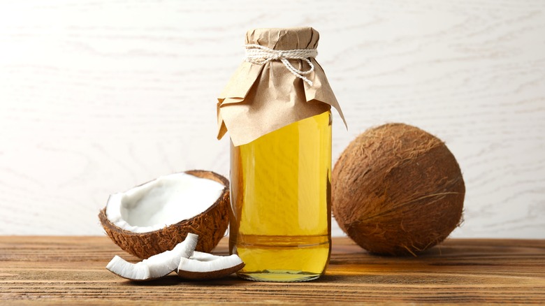 coconut oil in bottle next to coconuts