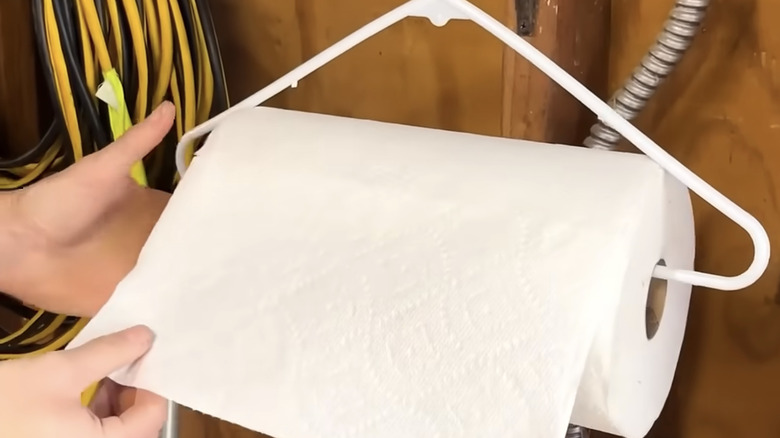 Hands holding a DIY paper towel holder hanging inside a shed.