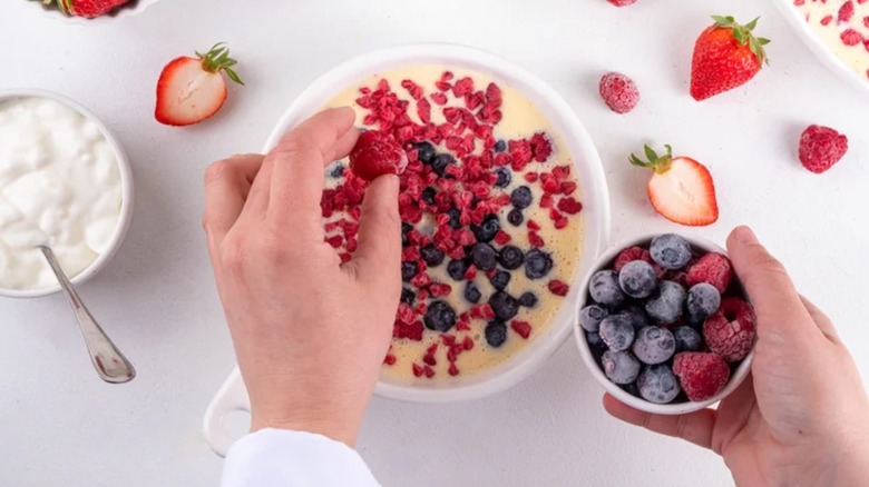 A white bowl of baked yogurt being topped with fresh berries