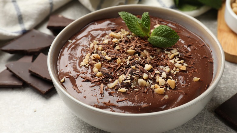 Chocolate mousse in a white bowl topped with nuts, chocolate shavings, and a mint sprig.