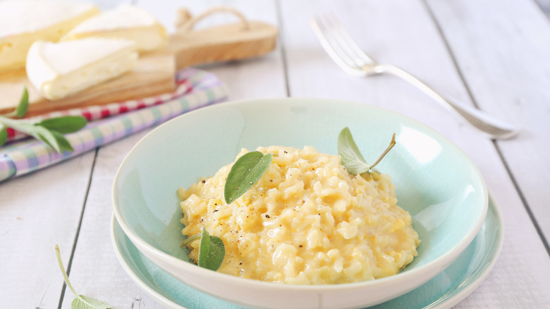 Creamy rice in a white bowl topped with fresh sage leaves