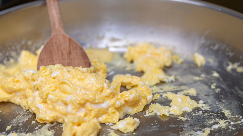 Scrambled eggs stirred  by a wooden spoon in a stainless steel pan