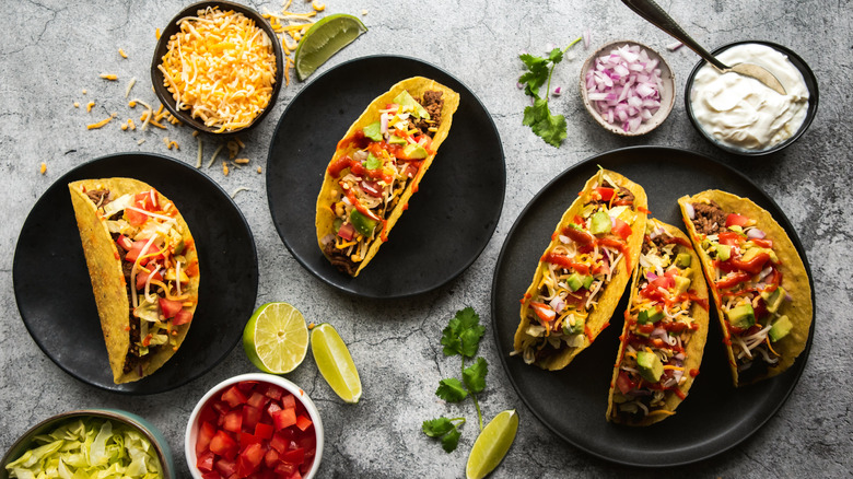 Hard shell tacos topped with cheese, onion, sour cream, and lime