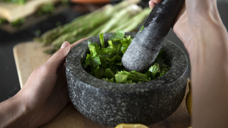 Hands working with a mortar and pestle and fresh herbs