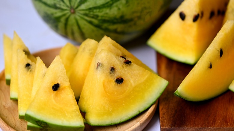 Yellow watermelon wedges with seeds on a wooden plate