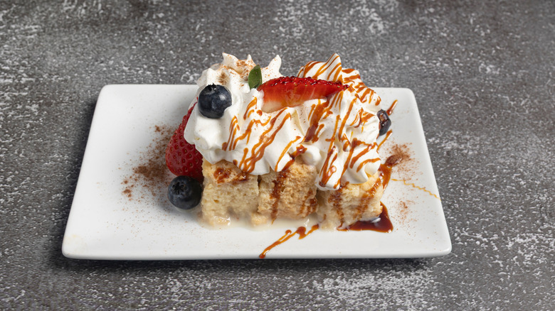 A square of tres leches cake garnished with berries, whipped cream, and caramel sauce