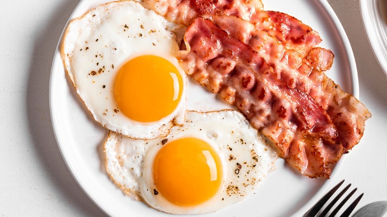 Crispy bacon and fried eggs on a white plate with a fork