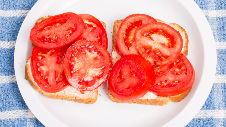 Two slices of bread with mayo and fresh tomatoes on a white plate