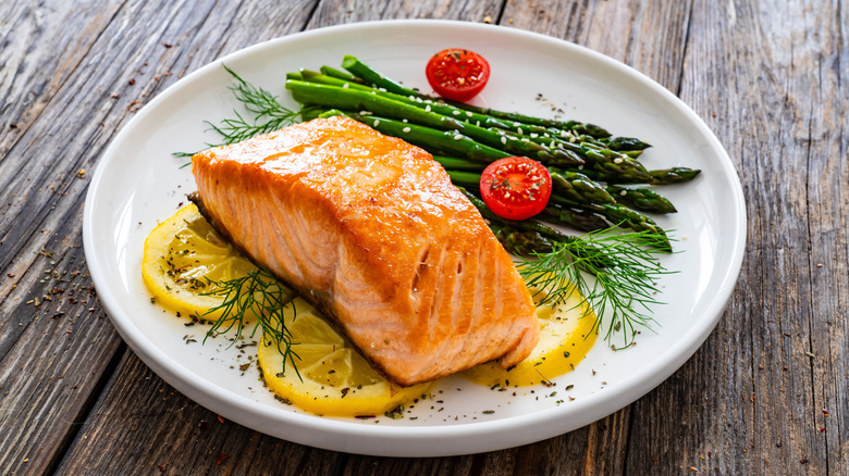 Salmon filet on lemon, dill, with asparagus on white plate