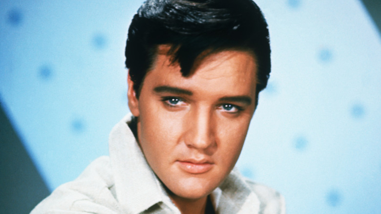 Elvis Presley poses in a white suit against a blue background