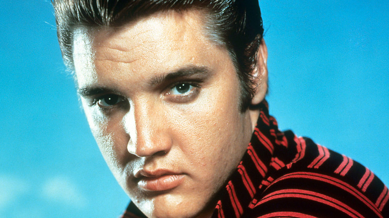 Portrait of Elvis Presley wearing striped red-and-black top against a blue background
