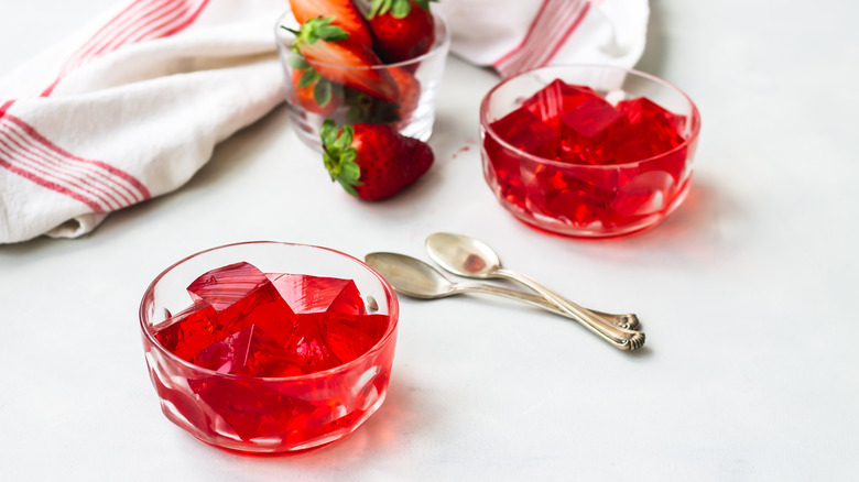 Strawberry flavored Jell-O cubes with fresh strawberries and spoons nearby.