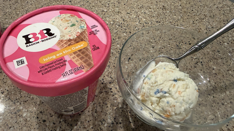 Baskin Robbins pint of Icing on the Cake with a scoop in a glass bowl with a spoon