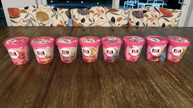 Eight flavors of Baskin Robbins ice cream on a wooden table with ice cream scooper