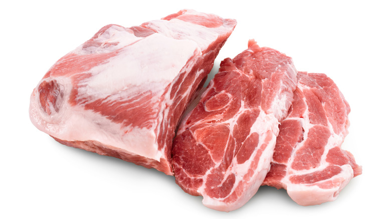 Raw pork shoulder with two pieces cut off on a white background