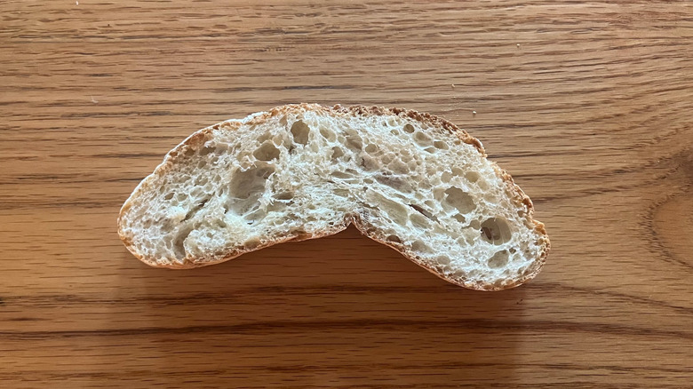 A bent slice of ciabatta sits on a wooden counter