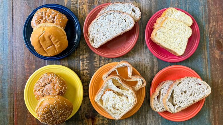 An overhead shot of a wooden table with six plates, each featuring two slices of a different type of bread from Aldi