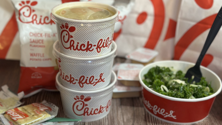 Chick-fil-A sides stacked in a pile of branded containers with a kale salad on the side with a fork