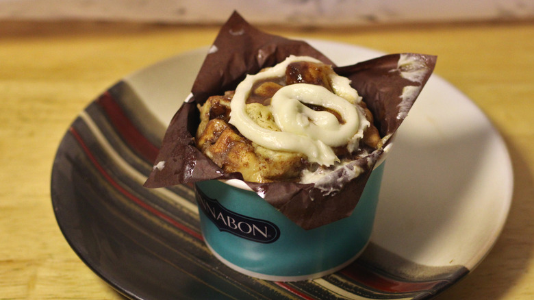 A cup of Cinnabon's Center of the Roll cinnamon bun pieces with icing on top set onto a plate