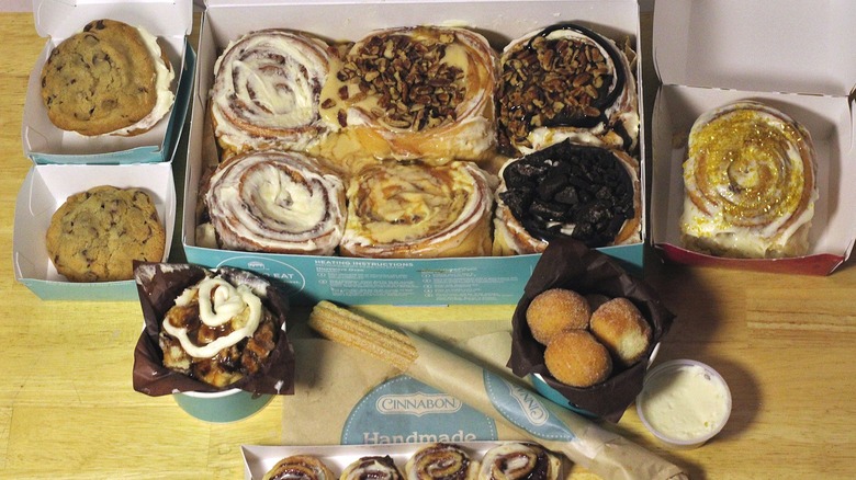 An array of menu items from Cinnabon featuring topped and classic cinnamon buns, cookies, churros, and other treats