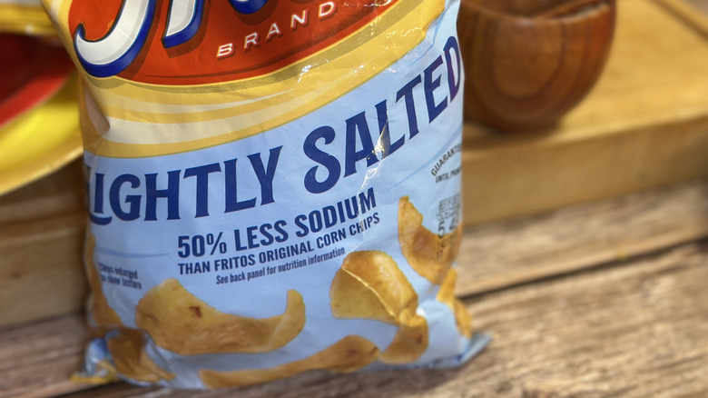 Bag of Lightly Salted Fritos on wooden surface in front of a salt crock