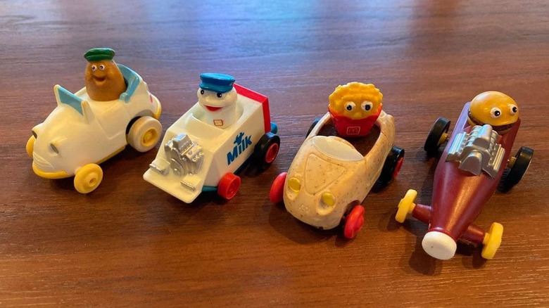 Four small car toys shaped like food sitting on a wooden table