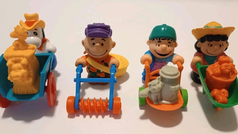Four figurines shaped like Peanuts characters, all pushing farming equipment