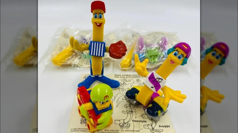 Three toys shaped like fries, wearing clothes, unwrapped but sitting on top of their instructions