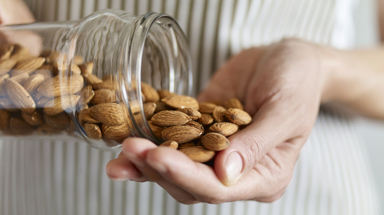 Almonds being poured from a glass jar into a hand