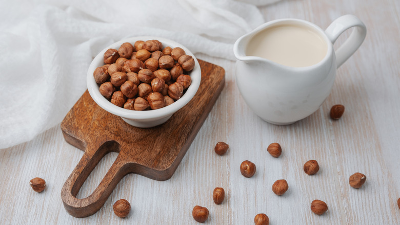 Hazelnut milk in white mug with hazelnuts in bowl on top of wooden serving tray