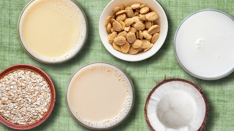 Assorted glasses of plant milk with bowls of nuts, oats, and half a coconut