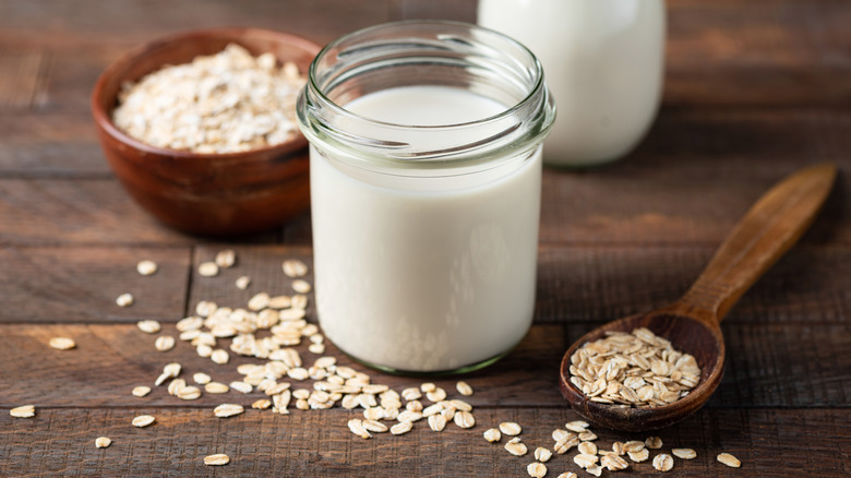 Oat milk in a glass jar on a table with oats scattered across the surface